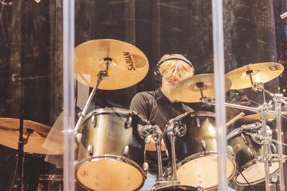 Drummer performing behind a drum kit with gold cymbals and drums on a dimly lit stage.