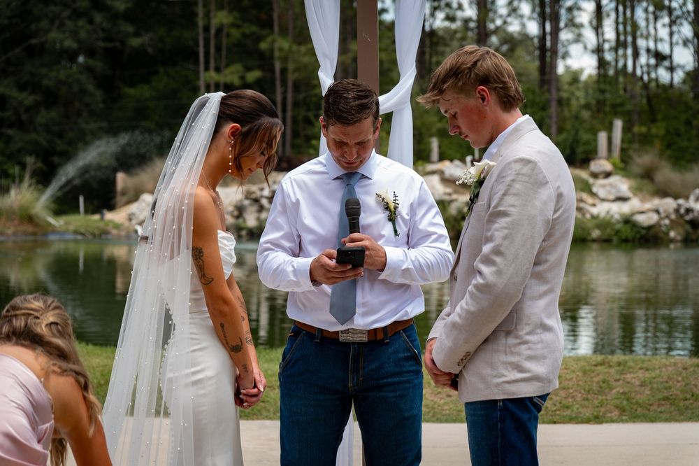 Outdoor wedding ceremony by a pond with bride, officiant reading vows, and groom in linen suit.
