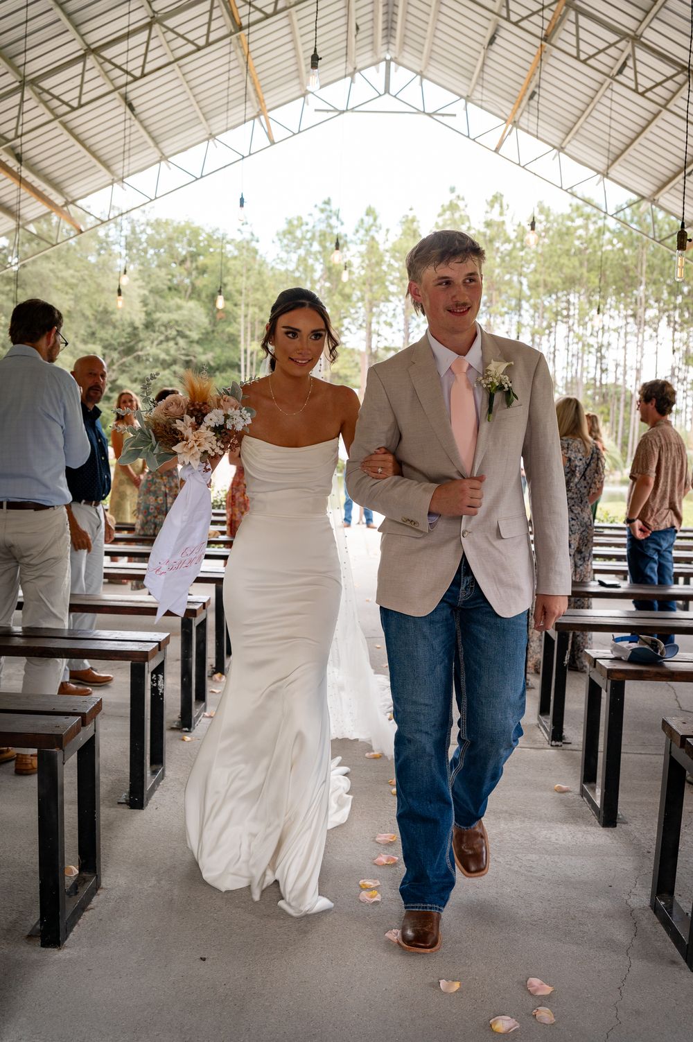 Bride and groom walk down aisle at outdoor wedding ceremony venue.