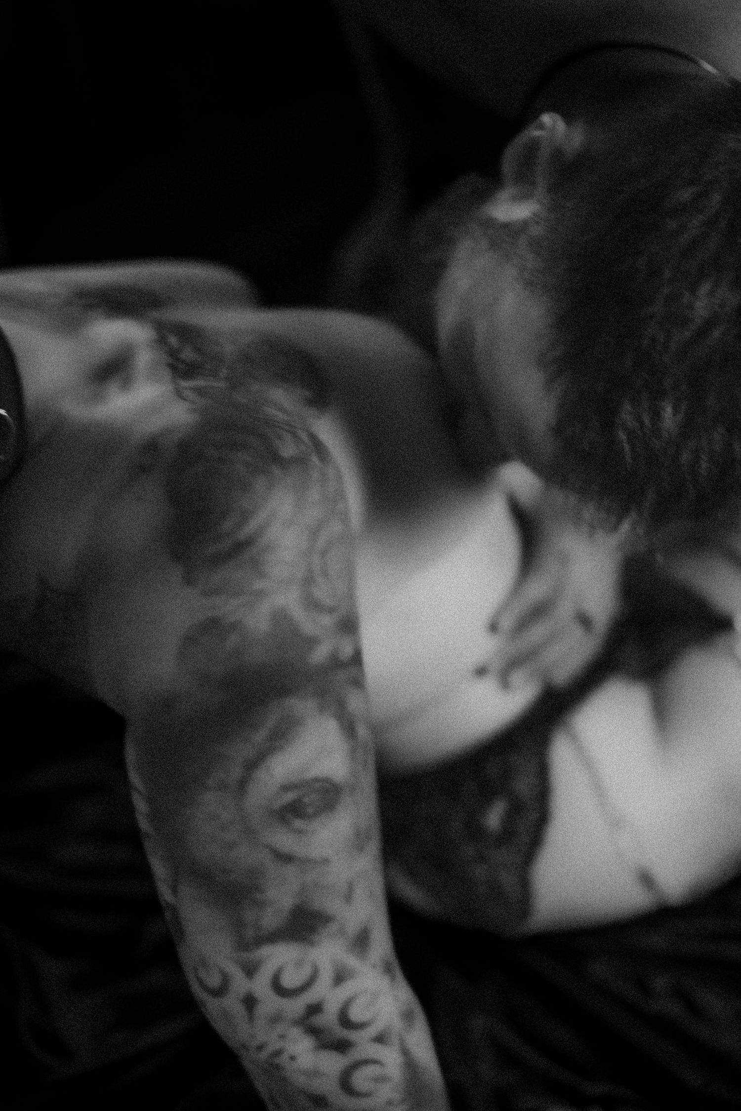 Tattooed couple in intimate embrace, woman in black lace lingerie, dark moody atmosphere.