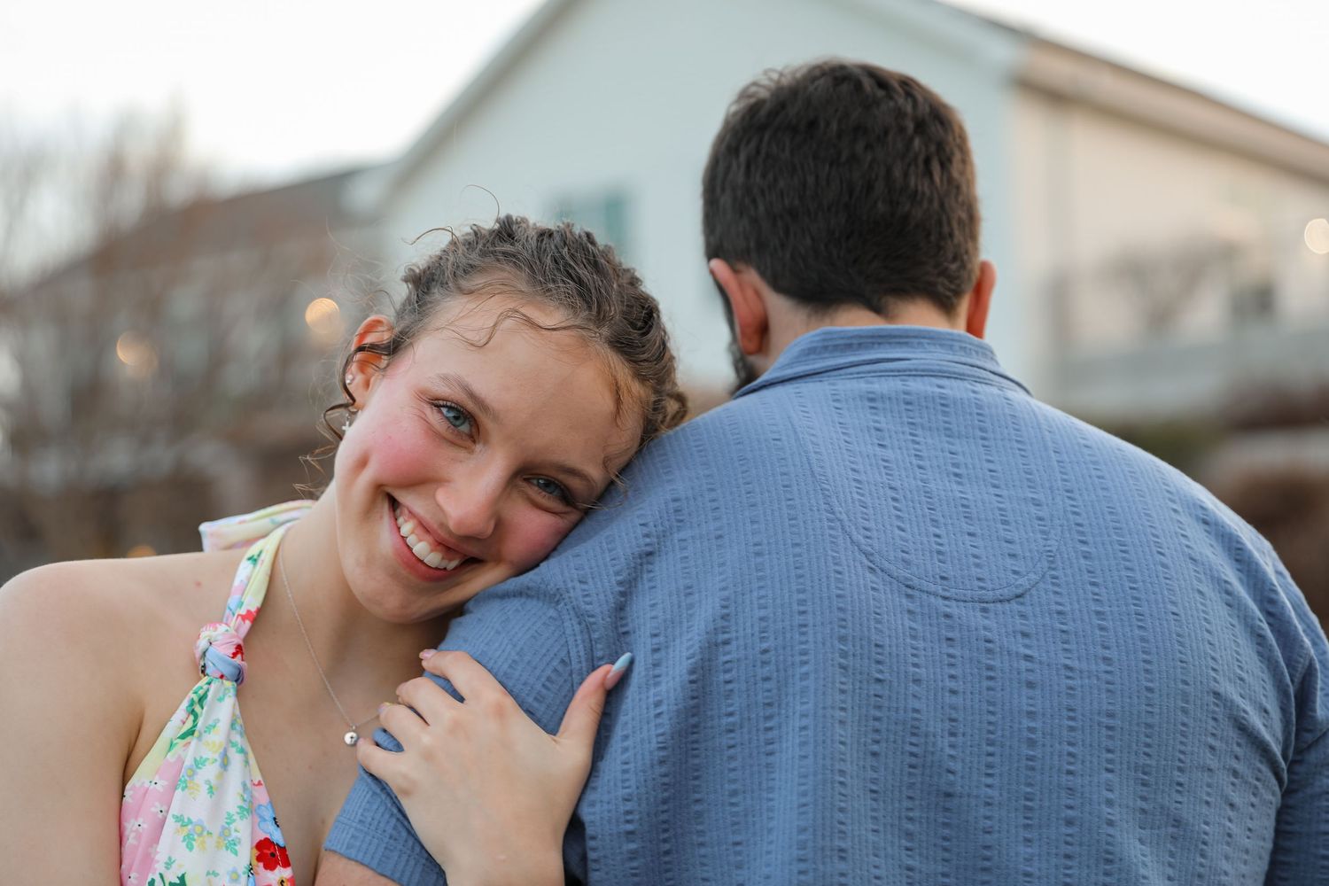 A couple sharing a romantic moment on a wooden deck, man kissing woman's cheek as she smiles under a blue sky.