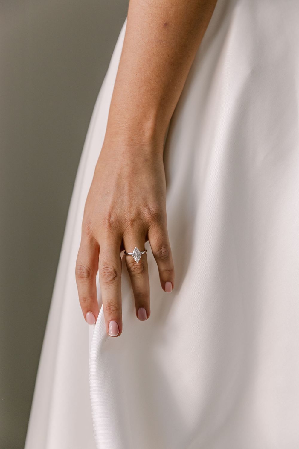 Close up of the bride's hand resting on her wedding dress, showcasing her engagement and wedding rings.