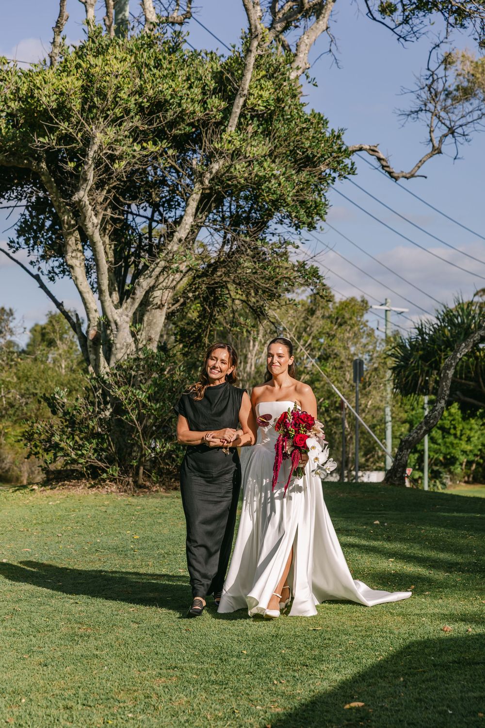 Bride walking down the aisle with a family member during an elegant outdoor wedding ceremony in Byron Bay.