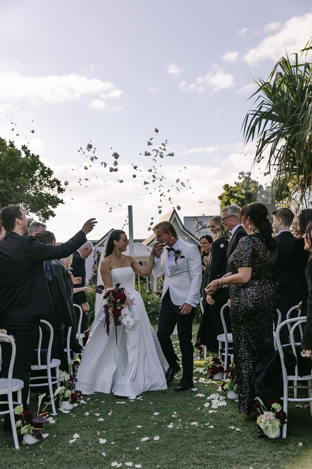 Bride and groom walking through a joyful confetti exit after their Byron Bay wedding ceremony.
