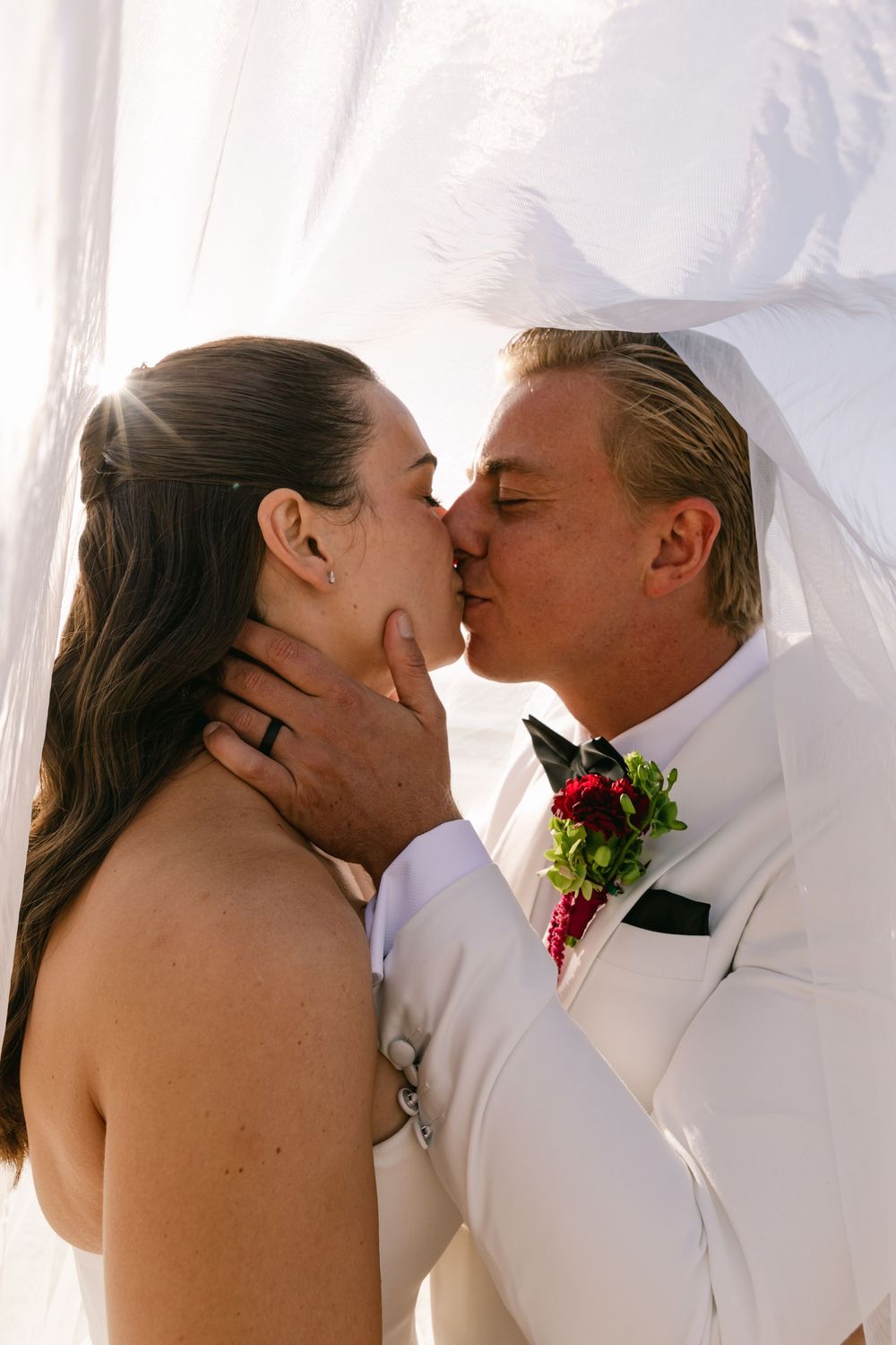 Bride and groom sharing a kiss beneath the bridal veil during their Byron Bay beach wedding.