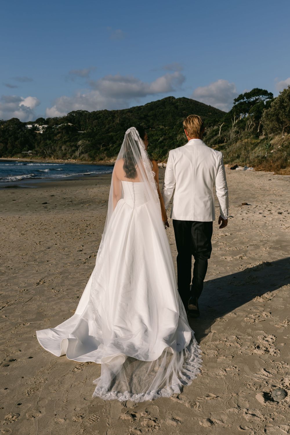 Bride and groom walking along the shoreline after their romantic Byron Bay beach wedding.