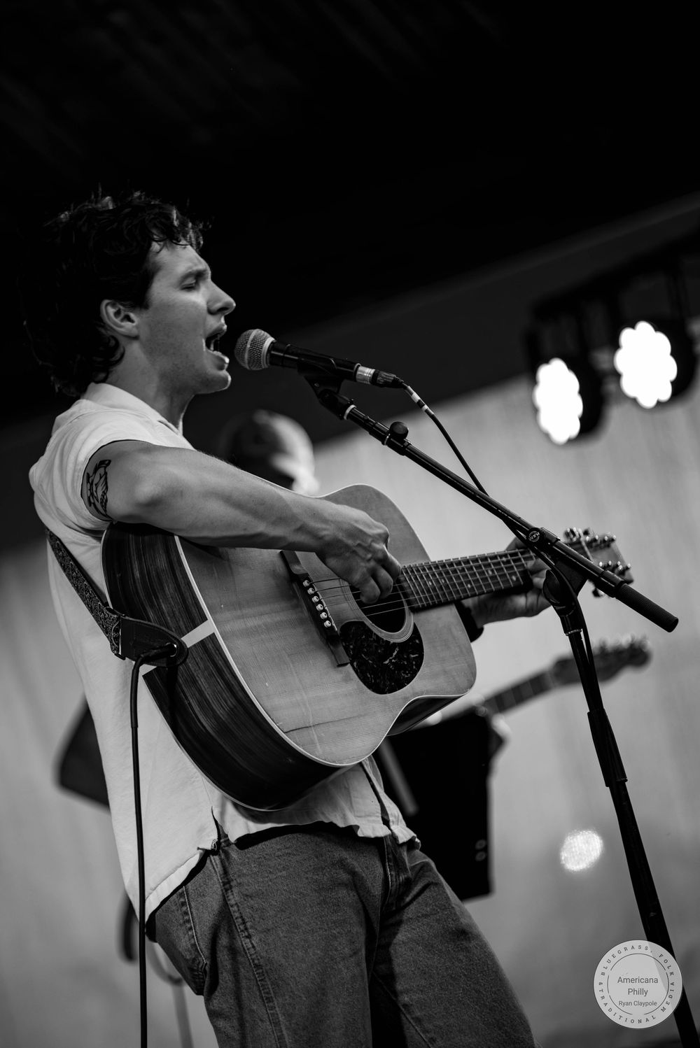 Young man passionately singing and playing acoustic guitar on stage in black and white concert photo.