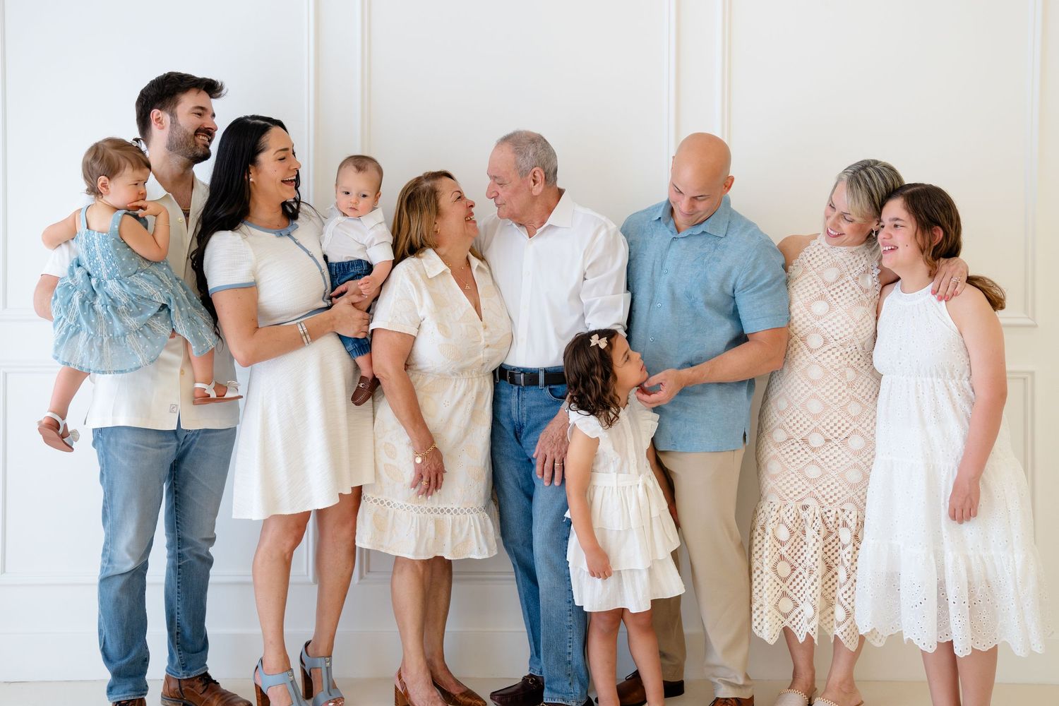 Multi-generational family portrait with adults and young children smiling together against a white background.