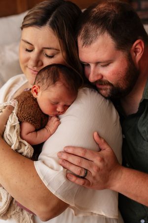 New parents tenderly cradle their sleeping newborn baby, sharing a loving family portrait moment.