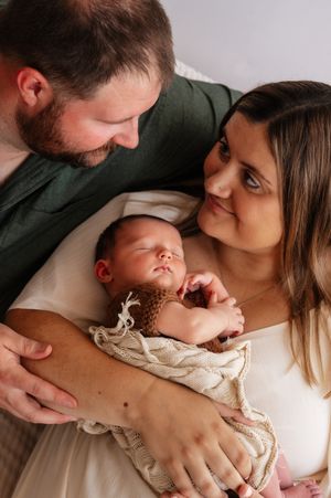 New parents lovingly gaze at their sleeping newborn baby wrapped in a cozy knit blanket.