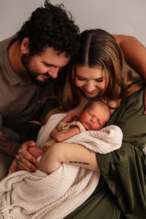 New parents lovingly gaze at their sleeping newborn wrapped in a white knit blanket during a studio photo session.