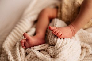 Close-up of tiny newborn baby feet and hands resting on a soft cream knitted blanket.