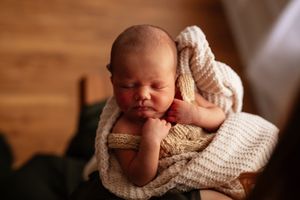 Peaceful newborn baby sleeping wrapped in a soft cream knit blanket, curled up in a cozy wooden bowl.