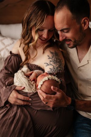 Happy couple smiling and cradling their newborn baby girl wearing a floral headband, captured in a warm lifestyle photography session.