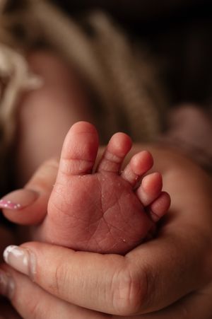 Close-up of a newborn baby's tiny foot cradled gently in a mother's hands with pink manicured nails.