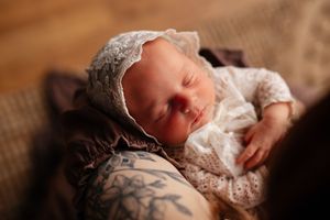 Sleeping newborn baby wearing a delicate white lace bonnet, cradled gently in soft warm light.