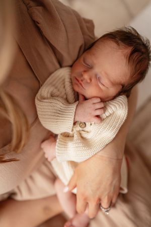 Sleeping newborn baby in cream knit outfit cradled in mother's arms during professional newborn photography session.