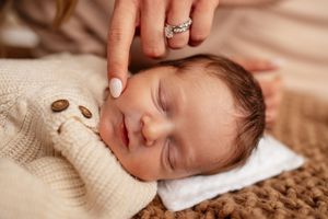 Peaceful newborn baby sleeping on a knit blanket while a mother gently touches their head with a ringed hand.
