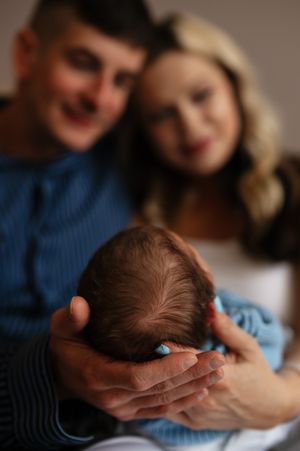 Parents lovingly hold their newborn baby, with the infant cradled gently in focus while the couple smiles softly behind.
