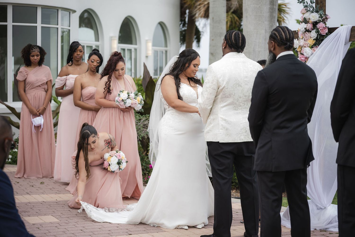Bridesmaid adjusting the bride's train during a front patio ceremony at the Mansion at Tuckahoe