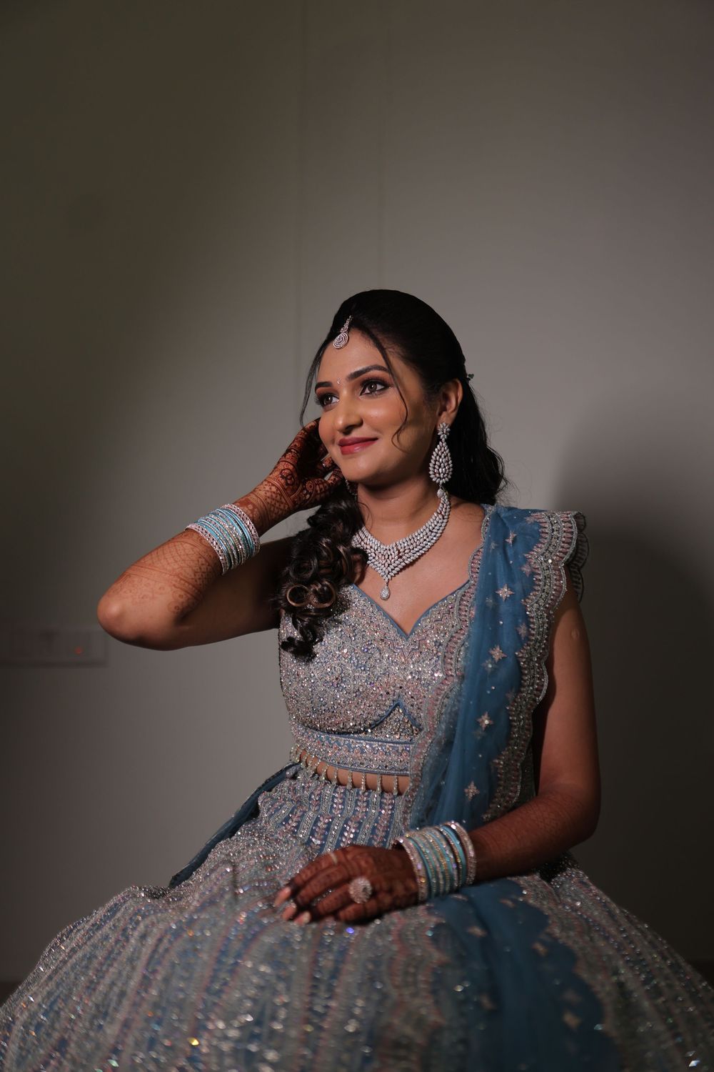 A bride in a sparkling blue lehenga with mehndi and diamond jewelry poses gracefully for a bridal portrait.