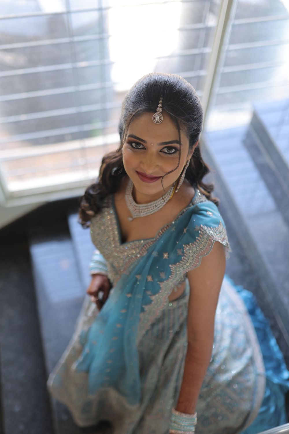 Woman in blue and silver embroidered saree with bridal jewelry smiles elegantly on stairs.