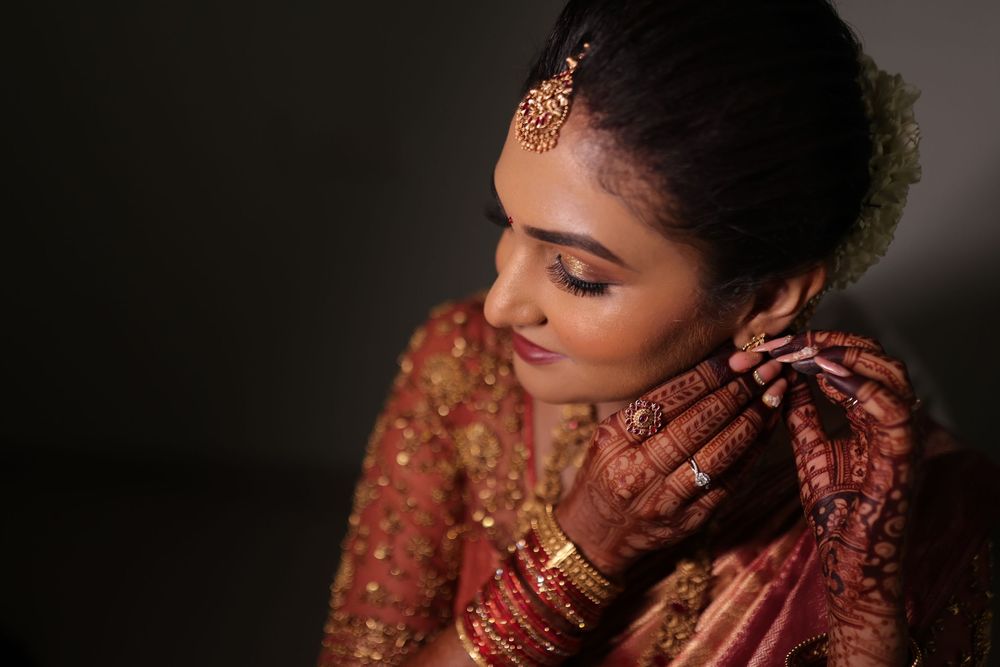 Indian bride in red lehenga adjusting earring, adorned with mehndi, gold bangles, and maang tikka jewelry.