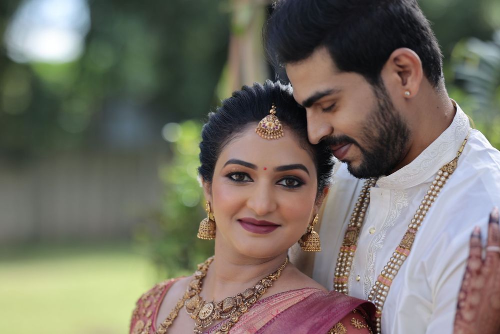 Indian bride and groom in traditional wedding attire, adorned with gold jewelry, posing together outdoors.