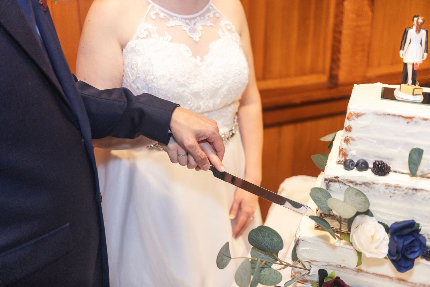 Bride and groom cutting a white wedding cake with blue roses and eucalyptus decorations at their reception.