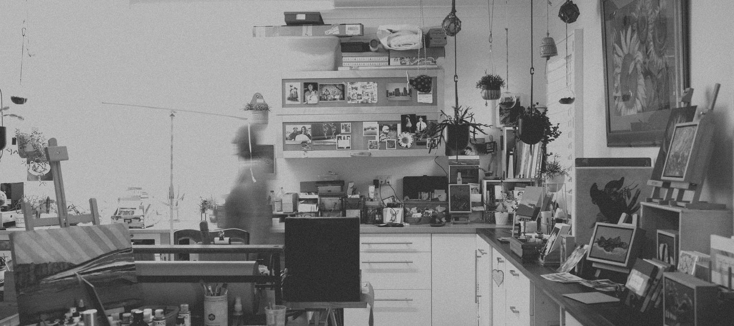 Black and white photo of cluttered artist studio workspace with shelves and equipment.