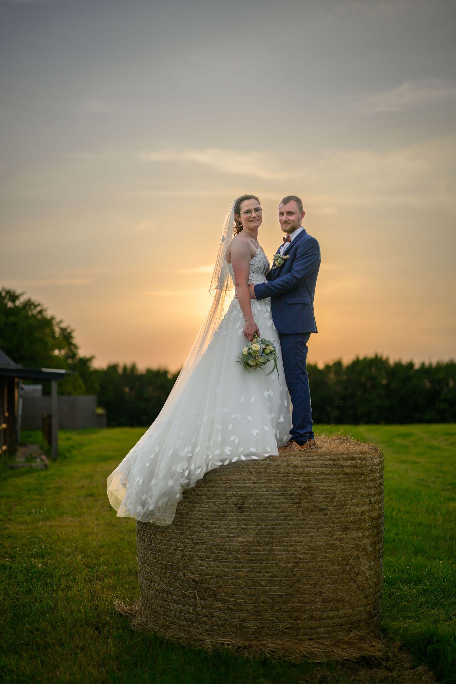 Photo de mariage, couleurs chaudes, couple sous un couché de soleil sur balot de paille à Monceau Saint-Waast en France
