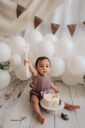 First birthday celebration with white balloons and cake on rustic wooden floor.在質樸的木地板上，用白色氣球和蛋糕慶祝寶寶一歲生日。