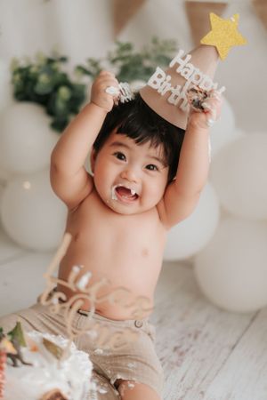 Joyful baby wearing birthday hat raises star decoration during celebration photo shoot.戴著生日帽的快樂寶寶在慶祝拍照時舉起了星星裝飾。