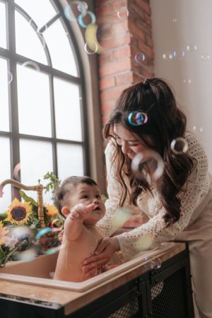 Mother and child playing with bubbles during bath time near arched window with brick wall.母親和孩子在拱形窗戶旁的磚牆邊洗澡時玩泡泡。