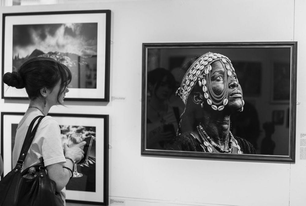 Black and white photo of a woman viewing African tribal portrait photography at an art gallery exhibition.