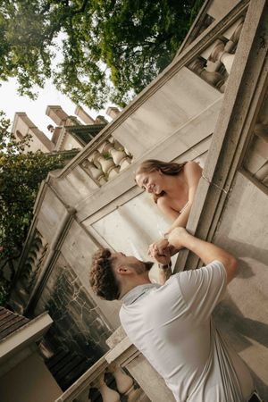 Romantic couple dancing outdoors near ornate stone balcony surrounded by lush green trees.