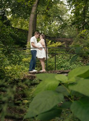 Couple sharing a romantic moment on a garden bridge surrounded by lush green trees and foliage.