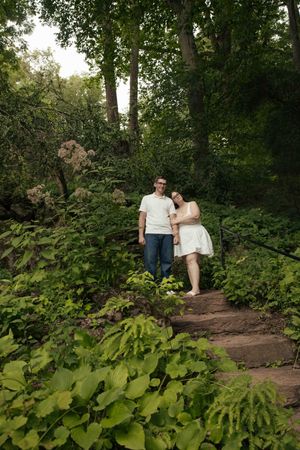 Couple poses on stone steps surrounded by lush green forest foliage during outdoor engagement session.
