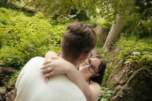 Couple embracing and smiling in a lush green garden setting near a tree.
