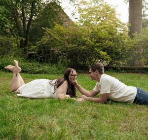 Couple lying on green grass in a park, smiling at each other on a sunny day.