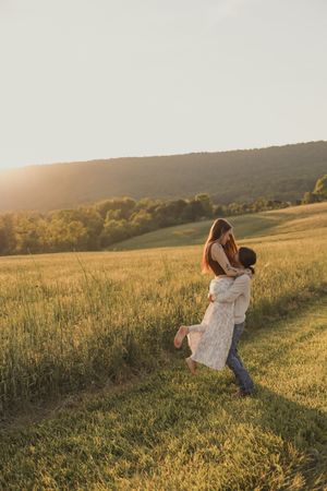 Couple embracing in golden sunset light in a scenic green meadow with rolling hills.