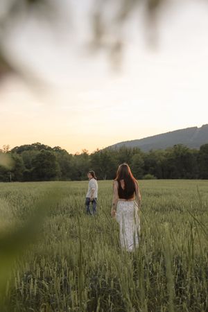 Couple walking through a lush green field at golden hour with mountain and trees in background.