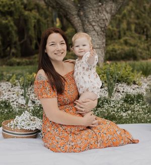 Happy mother in orange floral dress sits with her smiling toddler on a blanket in a blooming garden.
