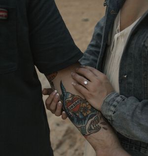 Close-up of tattooed hands holding with an engagement ring visible, romantic couple moment.