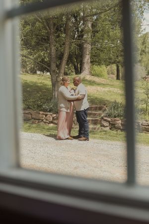 Couple dancing in garden viewed through rustic window frame on sunny day.