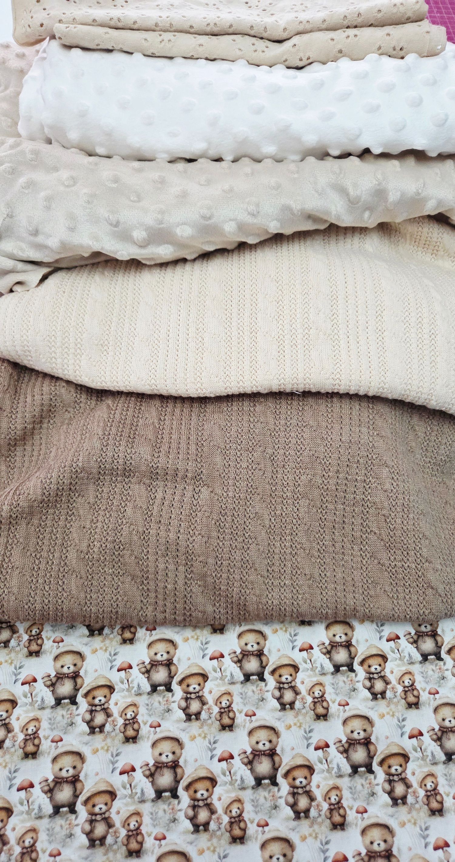 Stacked baby fabrics featuring minky dot, knit textures, and a cute bear mushroom print in neutral beige and brown tones.