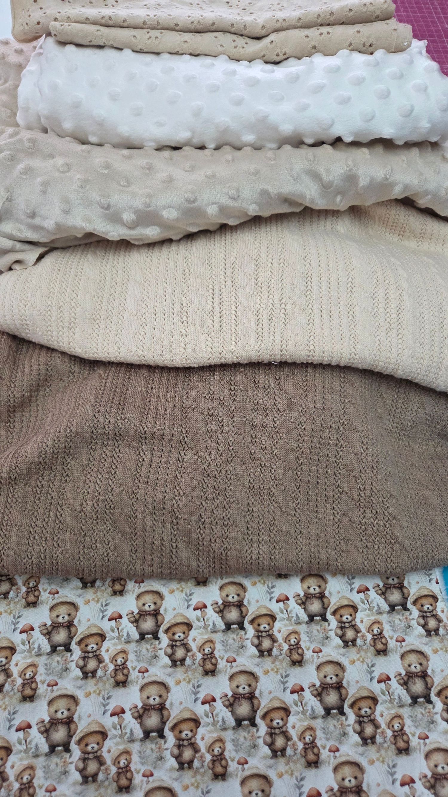 Stacked baby fabrics in beige and brown tones, including minky dot, knit, and a cute bear print fabric.
