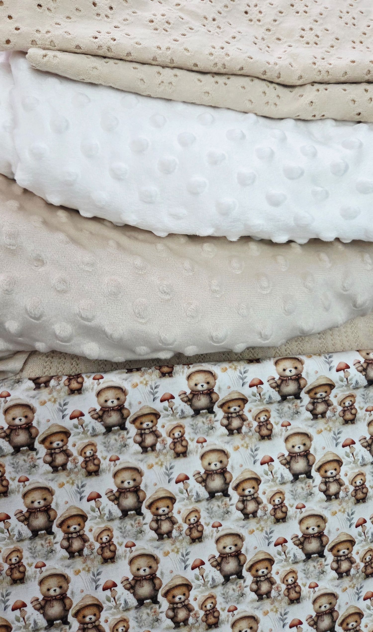 Stack of baby fabrics featuring teddy bear mushroom print, white minky dot, and beige floral materials for sewing projects.