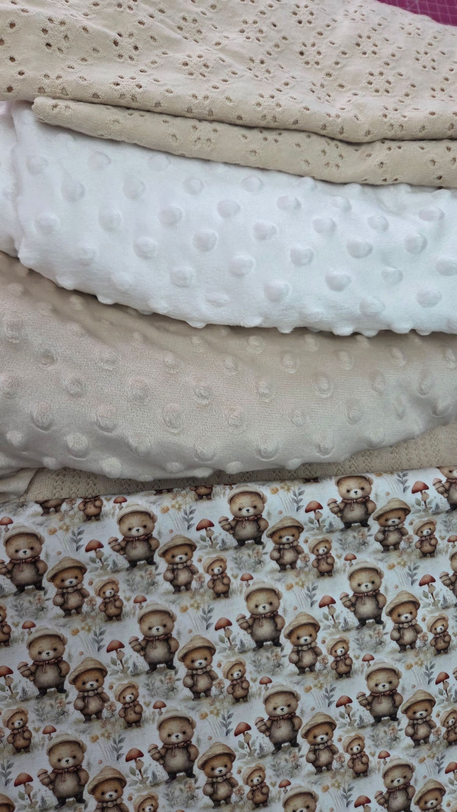 Stack of baby fabrics including beige eyelet, white minky dot, and bear mushroom print cotton fabric.