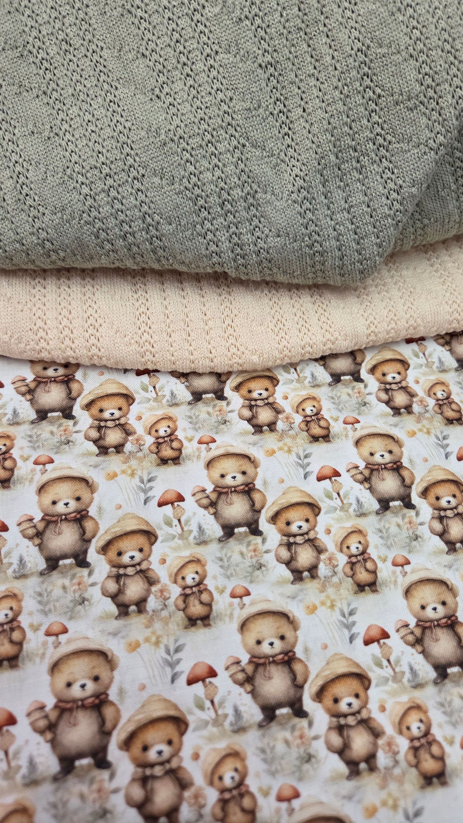 Stacked baby fabrics featuring cute teddy bear mushroom print, soft peach knit, and sage green textured blanket layers.